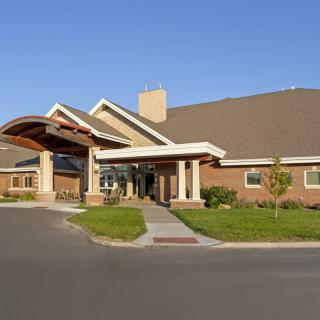 A brick building with a covered entrance and a landscaped driveway under a clear blue sky.