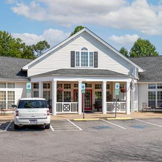 A white traditional-style building with a parking lot in front, under a partly cloudy sky.