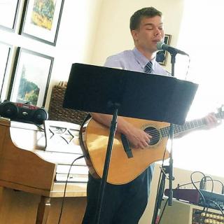 A person playing guitar and singing into a microphone indoors.