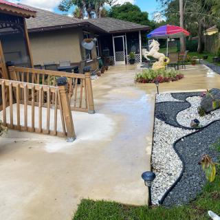 A backyard patio with a ramp leading to a garden area, featuring decorative landscaping and outdoor seating under a colorful umbrella.