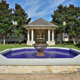 A scenic view of a fountain in front of a gazebo, surrounded by trees and greenery.