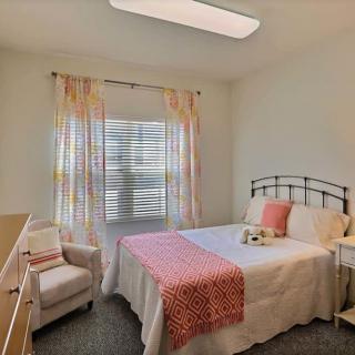 A cozy bedroom with a bed, crib, and chair near a window with colorful curtains.