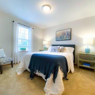 A cozy bedroom with a neatly made bed, two bedside tables with lamps, and a window letting in natural light.