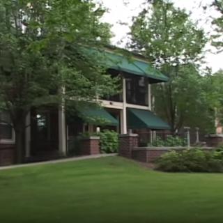 A two-story building surrounded by lush greenery and trees, featuring a well-maintained lawn.