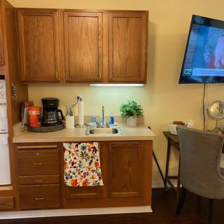 A cozy kitchenette with wooden cabinets, featuring a coffee maker and a wall-mounted TV.