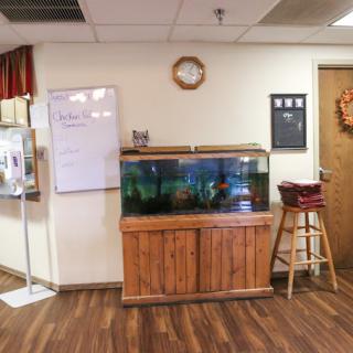 A room interior featuring a fish tank on a wooden stand, a whiteboard, and a stool.