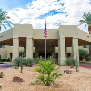 A hotel entrance with modern architecture, surrounded by palm trees and a desert landscape.