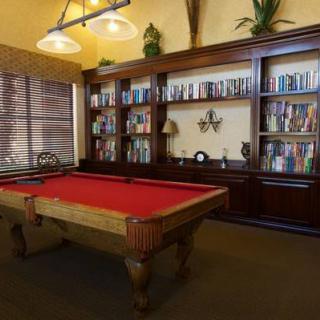 A luxurious library with a red felt pool table and wooden bookshelves filled with books.