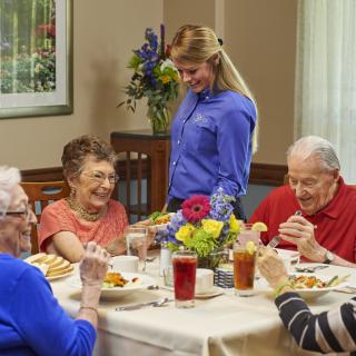 Elderly individuals enjoy a meal together in a restaurant setting with a waitress attending to them.