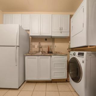 A compact laundry room with a washer, dryer, fridge, and white cabinetry.