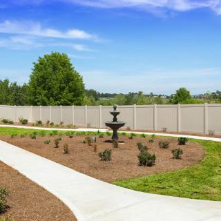 A well-maintained garden with a central fountain, surrounded by a fence and pathways.