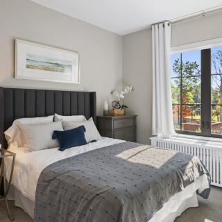 A modern and cozy bedroom with natural light streaming through a large window, featuring elegant decor and a neatly made bed.