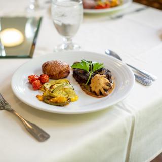 A gourmet meal featuring meat with sauce, vegetables, and a side, elegantly presented on a white tablecloth.