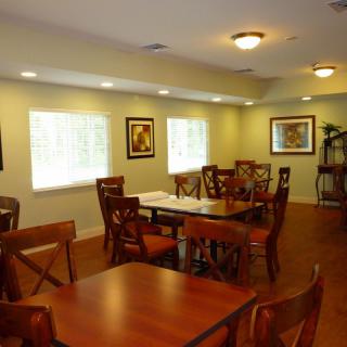 A cozy dining room with wooden tables and chairs, complemented by artwork on the walls and ample natural light.