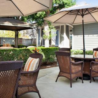 A cozy patio area with wicker chairs and tables under large umbrellas, surrounded by lush greenery.