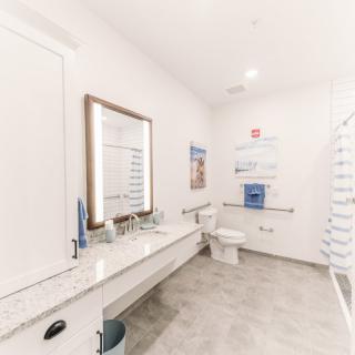 A modern, minimalist bathroom featuring a large mirror, sink, and toilet on a tiled floor.