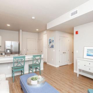 A modern apartment interior featuring a kitchen with bar stools and wood flooring.