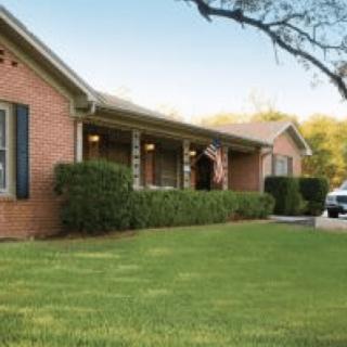 A brick house with a well-maintained lawn and a flag displayed on the porch.