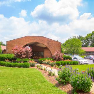 A well-maintained building surrounded by lush gardens and vibrant flowers under a bright blue sky.