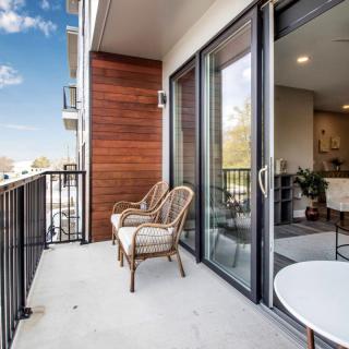A modern balcony with outdoor seating, featuring large glass doors and a view of the sky.