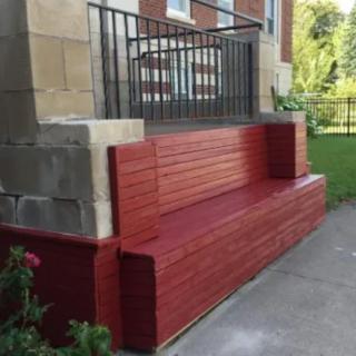 A red wooden bench built into porch stairs with black railings.