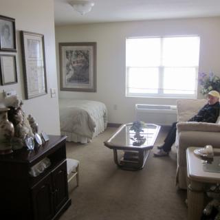 A cozy apartment space with a combined living and bedroom area, featuring comfortable seating and artwork on the walls.
