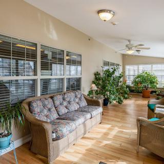 A cozy living room with a sofa, abundant indoor plants, and large windows letting in natural light.