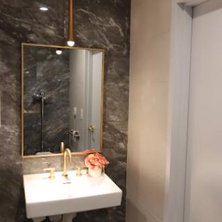 A stylish and modern bathroom featuring a marble wall, elegant mirror, and gold accents.