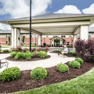A well-maintained building entrance with landscaped gardens and a paved walkway under a covered entry.