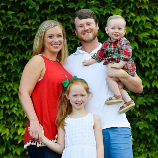 A happy family posing for a photo in front of green foliage.