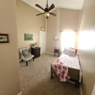 A cozy bedroom featuring a single bed with floral bedding, a chair, and a ceiling fan.