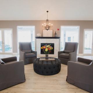 A modern living room with four gray chairs arranged around a central fireplace and a round ottoman.