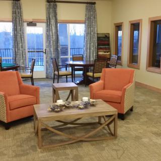 A cozy living room setup with two orange chairs, a wooden coffee table, and large windows with curtains.