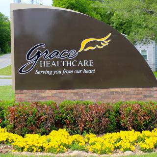 An outdoor sign for Grace Healthcare with a landscaped area featuring yellow flowers.
