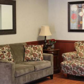 A cozy living room with a sofa, a patterned chair, and decorative elements like a lamp, mirror, and painting.