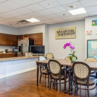 A communal kitchen and dining area featuring a table with chairs, a countertop with cabinets, and decorative flowers.