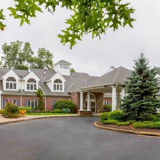 A large residential building with a landscaped driveway and trees surrounding the entrance.