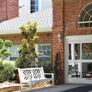 A building entrance with a white bench and greenery.