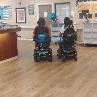 Two individuals in power wheelchairs navigating a healthcare facility.