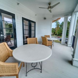 A cozy patio area with a round table and wicker chairs, featuring a ceiling fan and surrounded by glass doors.