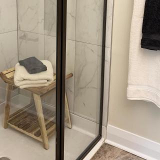 A minimalist bathroom with a glass shower door and a wooden stool holding towels.