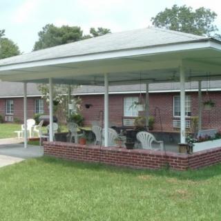 A covered outdoor patio area with seating and plants in front of a brick building.