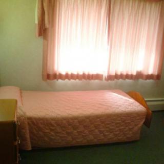 A small bedroom with a single bed featuring pink bedding and curtains.