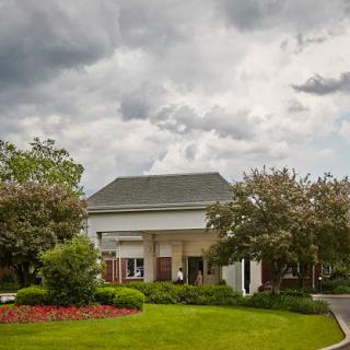 A modern building surrounded by well-maintained gardens under a dramatic cloudy sky.