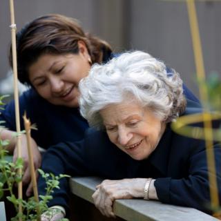An elderly woman enjoys gardening with the help of her caretaker.