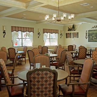 A cozy dining room with multiple tables and chairs, adorned with a chandelier and decorated windows.