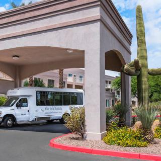 A hotel entrance with a shuttle bus parked nearby, surrounded by desert landscaping and a large cactus.