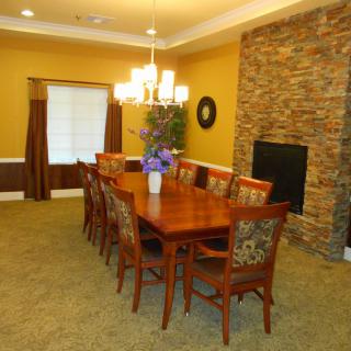 A well-appointed dining room featuring a long wooden table surrounded by chairs, a chandelier overhead, and a stone accent wall.