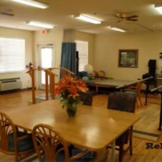 A well-lit room with rehabilitation equipment and a table with chairs and flowers.