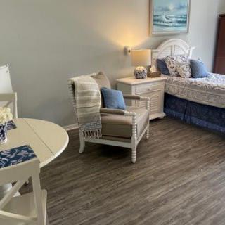 A cozy bedroom with coastal decor featuring a bed, armchair, small table, and warm lighting.